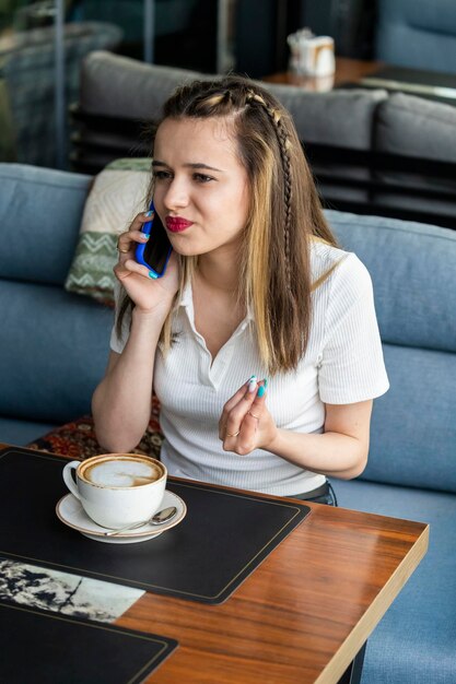 Vertical photo of young beautiful lady talking on the phone and sitting at the restaurant