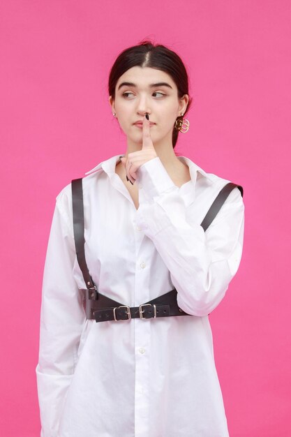Вертикальное фото юной леди прикладывает палец ко рту и думает на розовом фоне