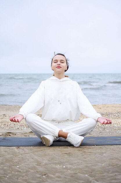 マットの上に座って、ビーチで瞑想をしている若い女性の垂直写真高品質の写真