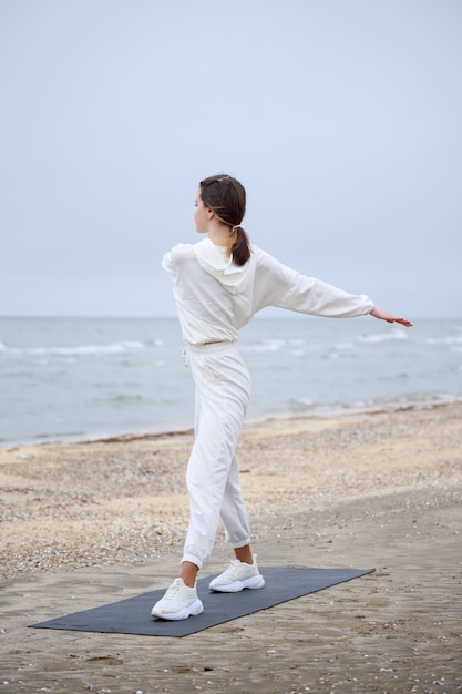 Vertical photo of young lady standing on at the beach and stretching her body High quality photo