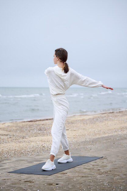 Вертикальное фото девушки, стоящей на пляже и растягивающей свое тело Фото высокого качества