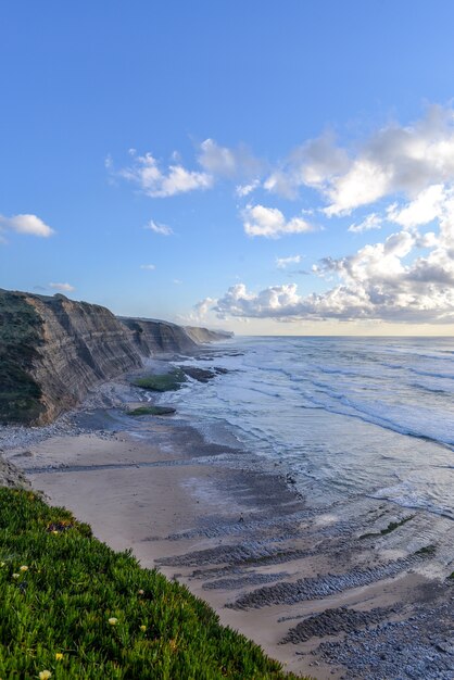 日光と曇り空の下、海と崖に囲まれたビーチの垂直方向の画像