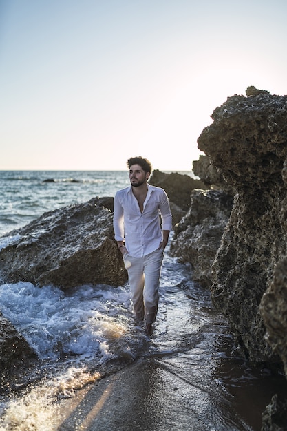 Vertical picture of a brunette male walking on the water next to the cliff