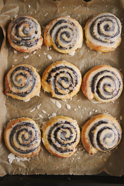 Free photo vertical picture of delicious poppy snail pastries with a sugar glaze in a tray on wooden table