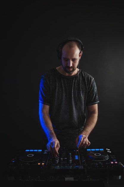 Vertical picture of a male DJ working under the lights against a dark background in a studio