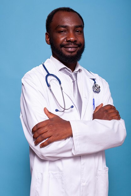 Vertical portrait of african american medical doctor with stethoscope posing confident wearing scrubs. Smiling medic in lab coat white uniform standing with arms crossed in studio.