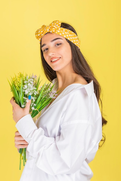 Ritratto verticale di bella signora che tiene mazzo di fiori e guardando la fotocamera su sfondo giallo foto di alta qualità