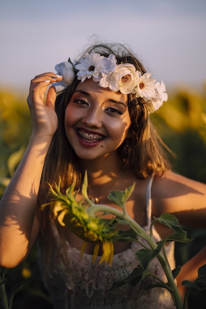 Vertical portrait brunette female in flower crow braces leaning forward smiling in sunflower field
