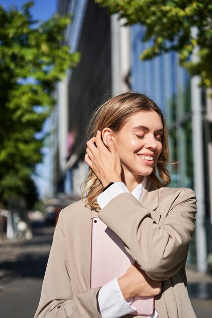 Vertical portrait of corporate woman holding digital tablet posing on street adjusting her hair and