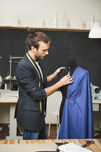 Foto gratuita ritratto verticale di maturo attraente talentuoso designer di abiti ispanici preparando abito blu per cucire, rimuovendo gli errori sul manichino, preparandosi per la sfilata di moda