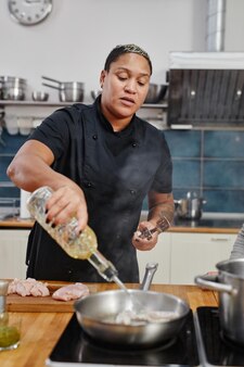 プロのキッチンで調理しながら肉を揚げる入れ墨の女性シェフの縦の肖像画