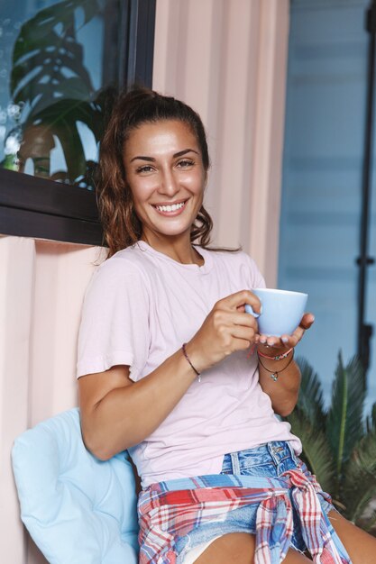 ポーチでお茶を飲むリラックスした笑顔の女の子の縦の肖像画。