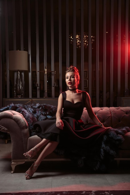 Vertical portrait of young beautiful girl wearing black dress and sitting on the sofa