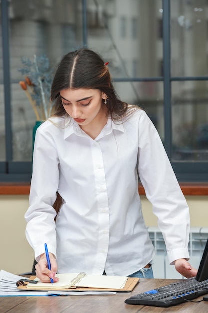 Vertical portrait of young businesswoman standing on at the office and writing notes