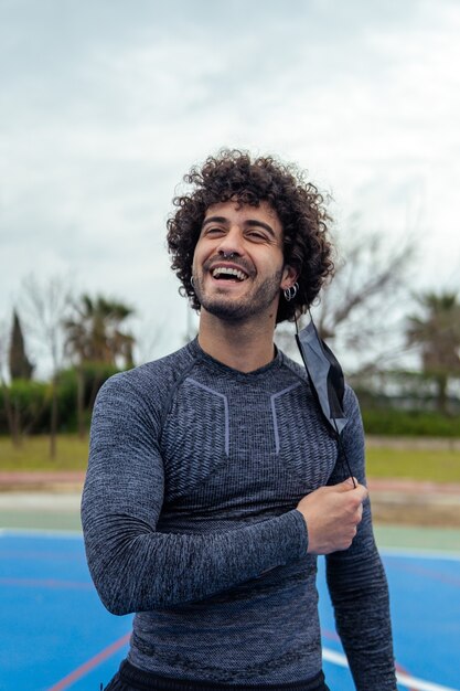 Vertical portrait of a young Caucasian athlete taking off his mask in the park