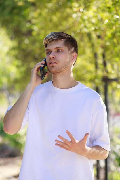 Tシャツを着て電話で話している若いハンサムな男の縦の肖像画高品質の写真