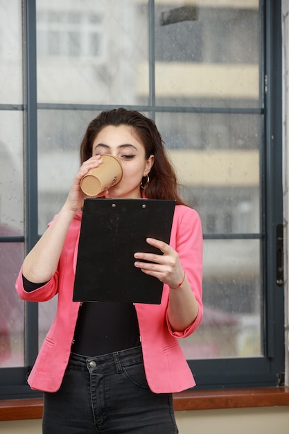 Ritratto verticale di una giovane donna che beve caffè e legge i suoi appunti