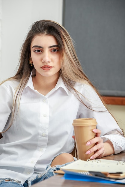 一杯のコーヒーを保持し、カメラを見ている若い女性の縦の肖像画