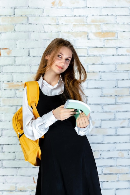 Вертикальный портрет молодой школьницы, держащей блокнот и смотрящей в камеру