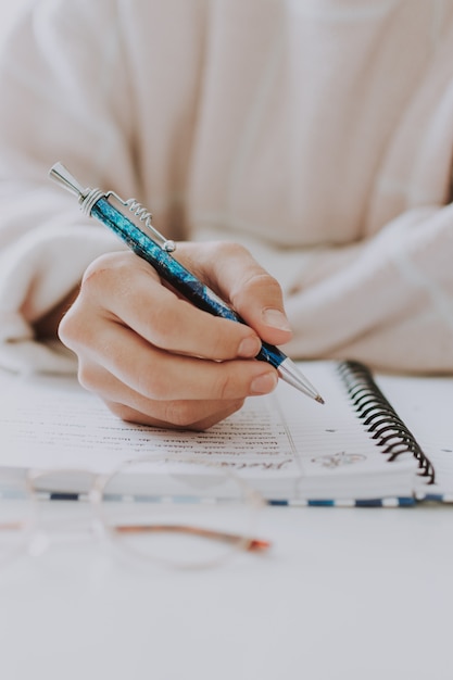 青のペンでノートに書く女性の垂直選択的なクローズアップ