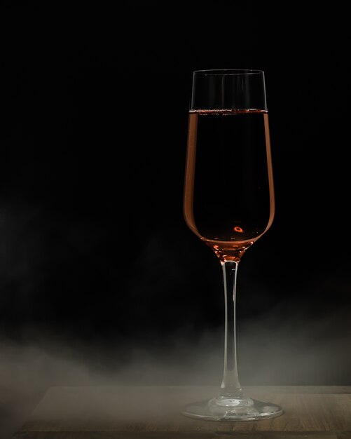 Vertical selective focus shot of a glass of champagne on a wooden surface and a black distance