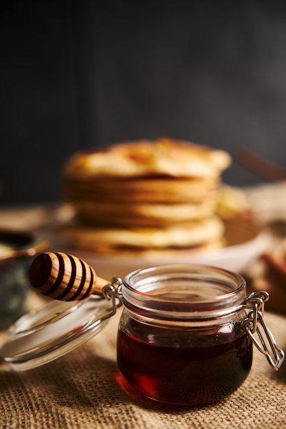 Vertical selective focus shot of a jar of honey with apple pancakes on the background