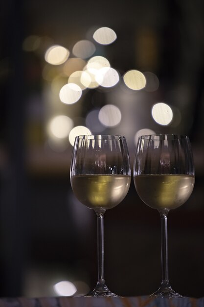 Vertical selective focus shot of two glasses of drink with the blurry lights in the background