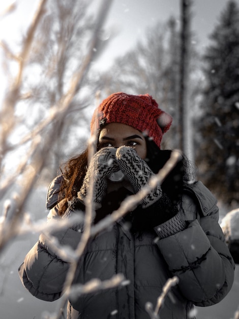 Vertical selective shot of a female wearing red hat, gloves and gray jacket during winter