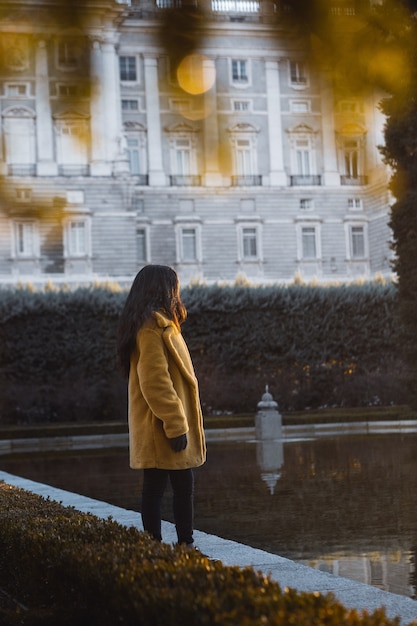 Colpo selettivo verticale di una femmina che porta cappotto giallo che fa una pausa l'acqua vicino ad una costruzione bianca