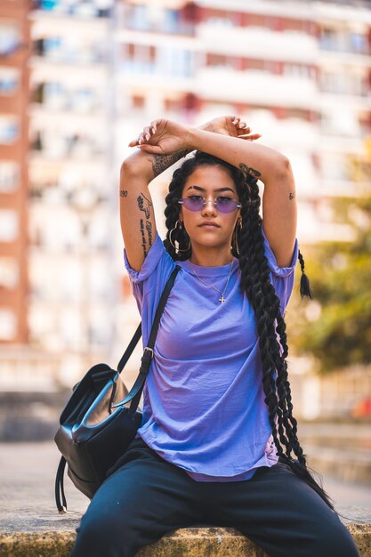 Вертикальный снимок афроамериканки с татуировками в фиолетовой рубашке и солнечных очках