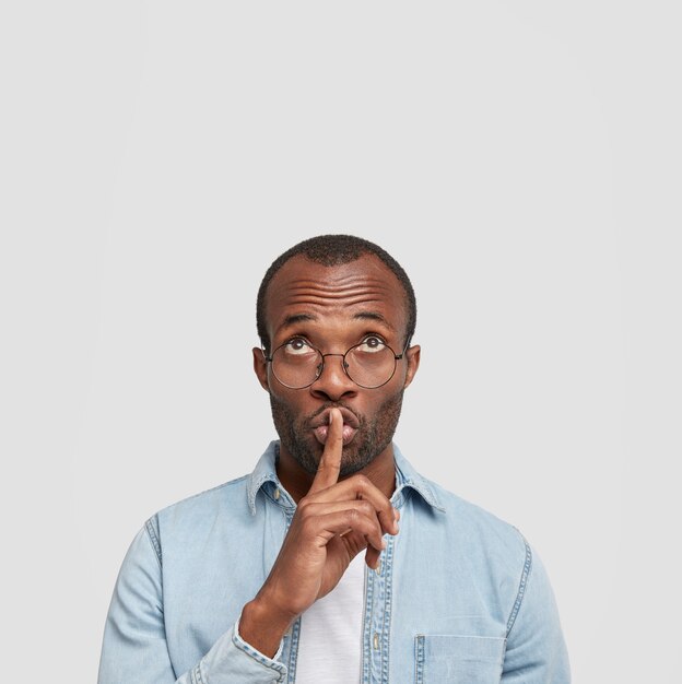 Vertical shot of African American male keeps fore finger as being mute