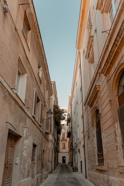 Vertical shot of an alleyway in the middle of buildings under a blue sky at daytime