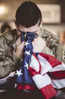 Free photo vertical shot of an american soldier mourning and praying with the american flag in his hands