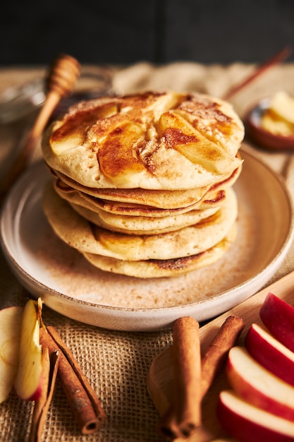 Vertical shot of apple pancakes on a plate with apple slices and cinnamon on the side