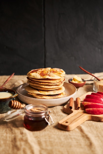 Вертикальный снимок яблочных блинов на тарелке с кусочками яблока, медом и ингредиентами сбоку