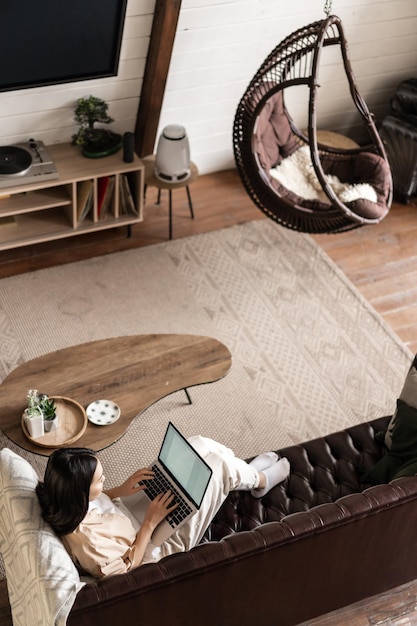 Vertical shot of asian girl student studying at home on sofa laying on couch and using laptop computer