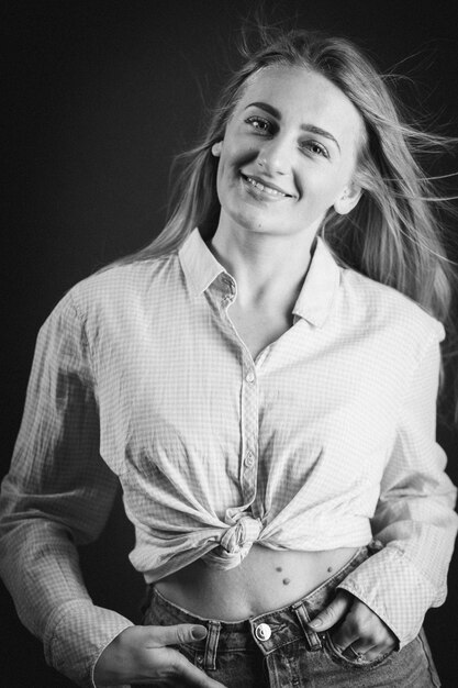 Vertical shot of an attractive blonde female in jeans and a short shirt posing on a black wall