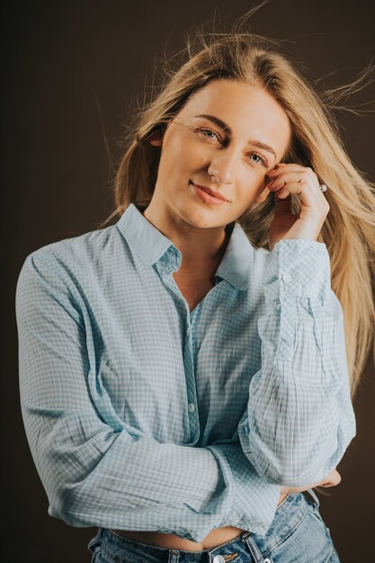 Vertical shot of an attractive blonde female in jeans and a short shirt posing on a brown background