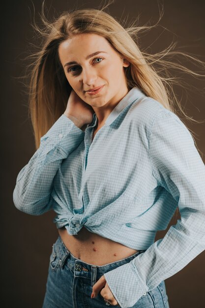 Vertical shot of an attractive blonde female in jeans and a short shirt posing on a brown background