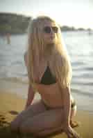 Free photo vertical shot of an attractive female wearing a black bikini sitting on the beach