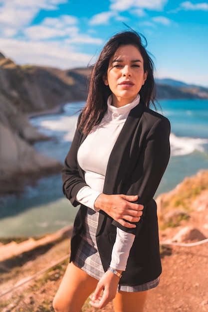 Vertical shot of an attractive stylish Hispanic female posing on a seacoast in Zumaia, Gipuzkoa