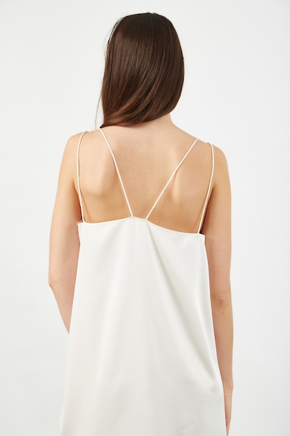 Вертикальный снимок спины девушки в легком белом платье под светом в студии
