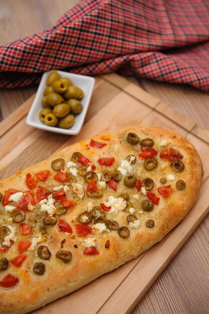 Vertical shot of a baked bread made with olives and tomatoes and served on a wooden board