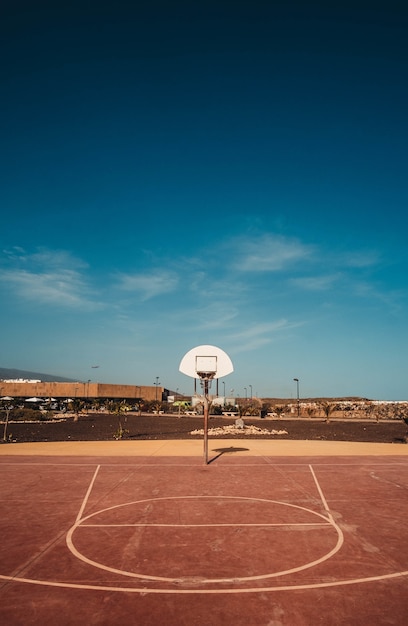 Vertical shot of a basketball court with the hoop visible under the blue sky