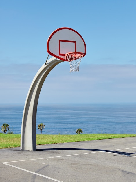 Вертикальный снимок баскетбольного кольца у моря под красивым голубым небом