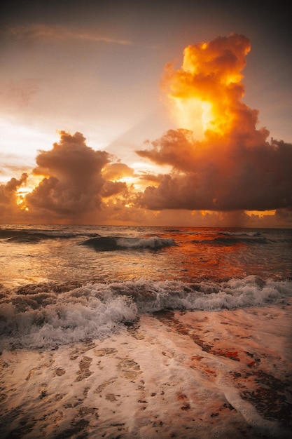 美しい夕日の中で曇り空の下で海の波に囲まれたビーチの垂直ショット