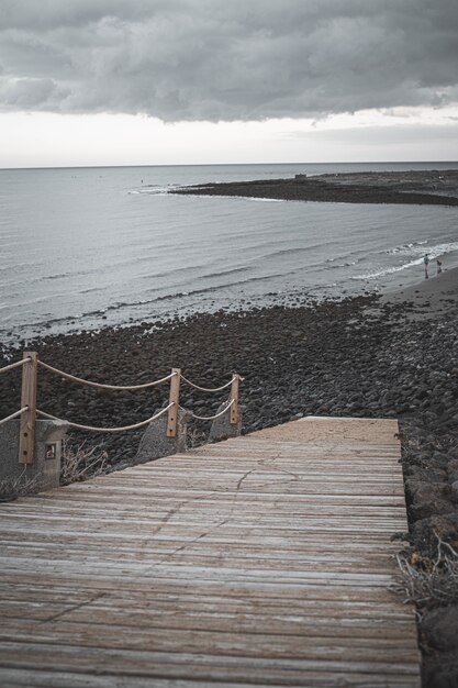 Vertical shot of a beach with a wooden bridge  under cloudy sky