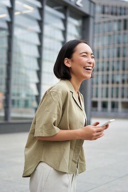 Free photo vertical shot of beautiful asian woman walking on street laughing and looking happy enjoying the day