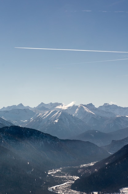 Vertical shot of beautiful mountain ranges under a bright sky with engine trails