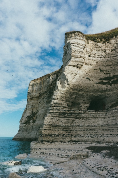 Vertical shot of a beautiful rocky cliff by the peaceful sea during daytime